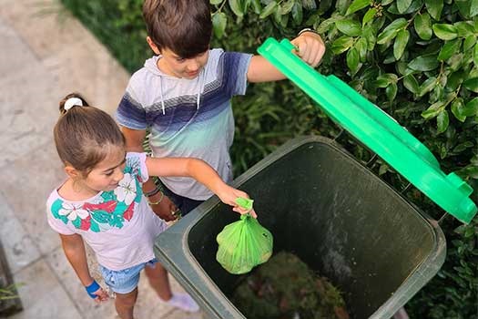 Two kids putting a green compostable bag into a green bin