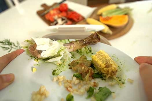 Assorted food scraps being scraped off a plate into kitchen caddy