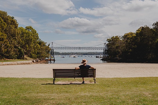 Man sitting on park bench overlooking the water and Parsley Bay suspension bridge